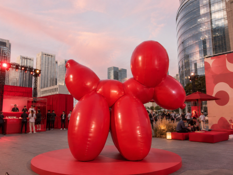 Large red inflatable balloon dog sculpture displayed at a contemporary outdoor brand event