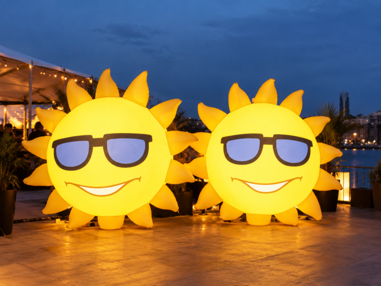 Two illuminated inflatable sun figures with sunglasses displayed at an evening outdoor event